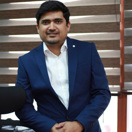 A portrait of a smiling man in a blue suit, identified as Dr. Ashish Dubey.